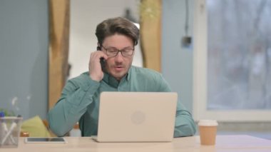 Mature Adult Businessman Talking on Phone while using Laptop