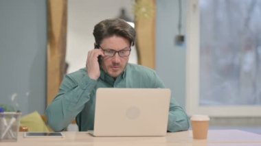 Displeased Mature Adult Businessman Talking Angrily on Smartphone in Office
