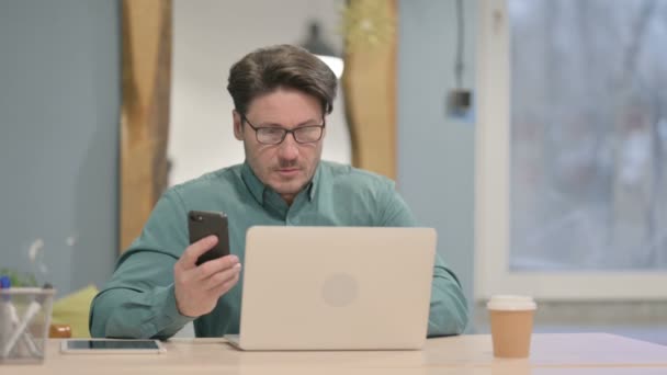 Mature Adult Businessman Using Smartphone While Using Laptop — Vídeos de Stock