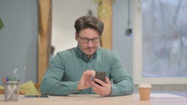 Mature Adult Businessman Browsing Internet on Smartphone in Office