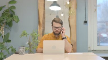 Middle Aged Businessman Talking on Phone while using Laptop