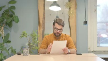 Middle Aged Businessman Celebrating Success while Reading Documents at Work