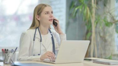 Young Doctor Talking on Phone while using Laptop