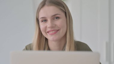 Dizüstü bilgisayar kullanırken Kameraya Gülümseyen Sarışın Genç Kadın 'ı Kapat