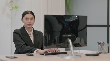 Genç İşkadını Masaüstü Bilgisayarı kullanırken Kameraya Bakıyor