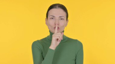 Young Woman with Finger on Lips Asking for Silence on Yellow Background