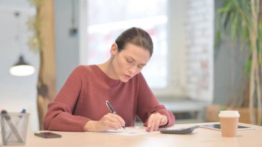 Evrak işleri yaparken hesaplama yapan genç bir kadın.