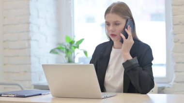 İş kadını dizüstü bilgisayar kullanırken telefonla konuşuyor