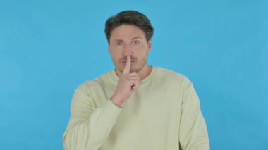 Handsome Young Man with Finger on Lips Asking for Silence on Blue Background