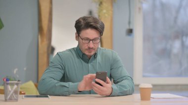 Mature Adult Businessman Browsing Internet on Smartphone in Office