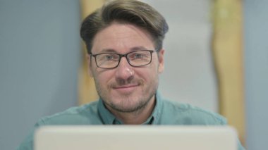 Close Up of Businessman Smiling at Camera while using Laptop