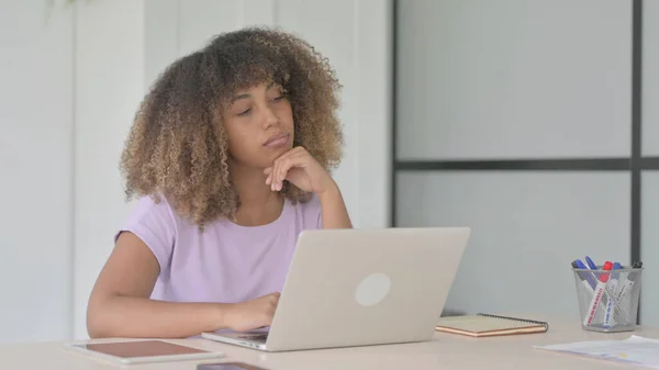 African American Woman Thinking while Working on Laptop in Office