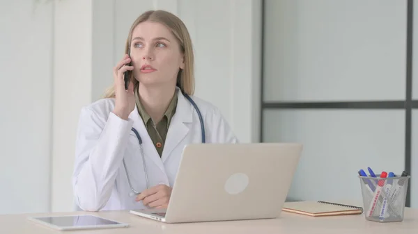 Lady Doctor Talking on Phone while Working on Laptop