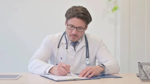 Middle Aged Doctor Writing Medical report, Paperwork
