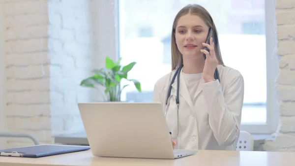 Young Female Doctor Talking on Phone while using Laptop