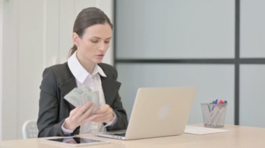 Businesswoman Counting Dollar while Working on Laptop
