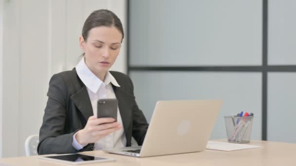 Bizneswoman Korzystająca Smartfona Podczas Korzystania Laptopa — Wideo stockowe