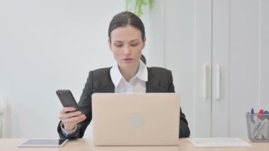 Young Businesswoman using Smartphone while using Laptop