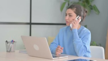 Laptop kullanırken telefonda konuşan Hintli kadın