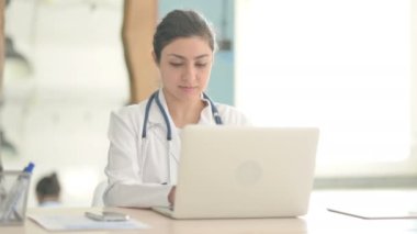 Laptop kullanırken kameraya bakan genç Hintli doktor