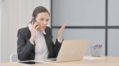Displeased Businesswoman Talking Angrily on Smartphone at Work