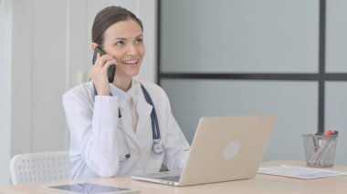 Young Doctor Talking on Phone while using Laptop