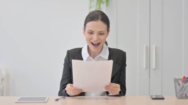 Young Businesswoman Celebrating Success while Reading Documents in Office