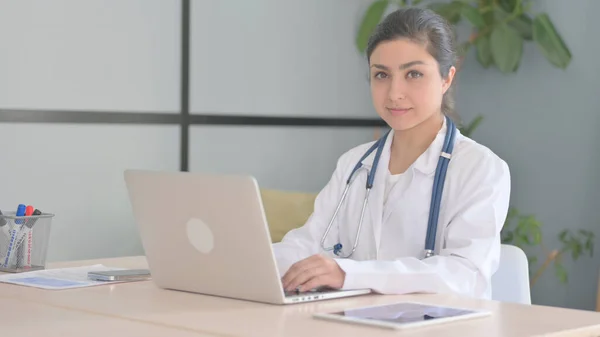 Young Indian Doctor Looking at Camera while using Laptop