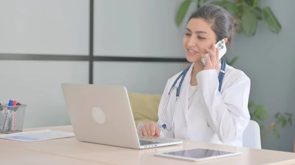 Young Indian Doctor Talking on Phone while using Laptop