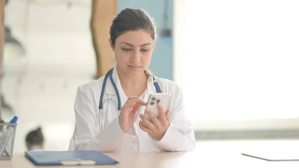 Young Indian Doctor Browsing Smartphone in Clinic