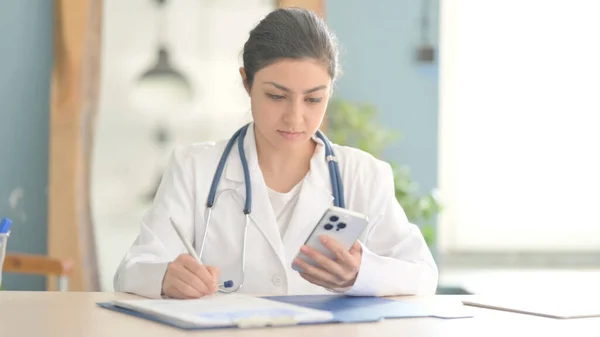 Young Indian Doctor using Smartphone for Paperwork