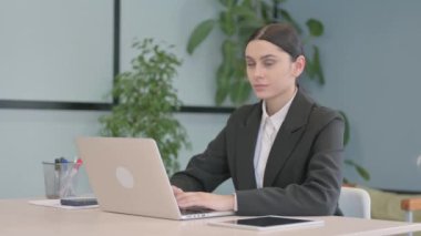 Dizüstü bilgisayarda çalışan genç iş kadını Kameraya doğru bakıyor