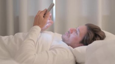 Yetişkin Adam 'ın Yataktaki Akıllı Telefon' da Başarı Kutlaması Yan Görünümü