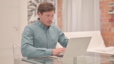 Olgun Yetişkin Adam Bilgisayarda çalışıyor Kameraya doğru bakıyor