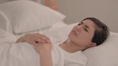 Baş ağrısı olan genç bir kadın yatakta yatıyor.
