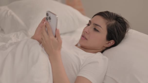 躺在床上时在智能手机上丢失的年轻女子震惊了 — 图库视频影像