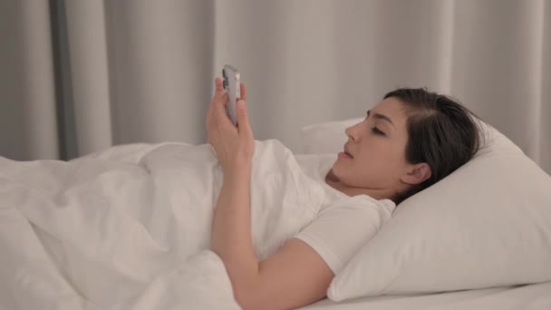 年轻女子在床上用智能手机庆祝成功的侧视图 — 图库视频影像