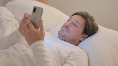 Yetişkin Adam yatakta yatarken akıllı telefon kullanıyor.
