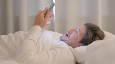 Yetişkin Adam 'ın Yataktaki Akıllı Telefon' da Başarı Kutlaması Yan Görünümü