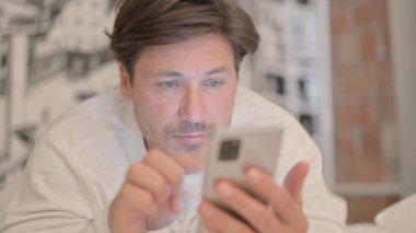 Yetişkin Adam 'ın karnının üstünde yatarken akıllı telefon kullanmasını kapat.