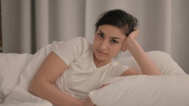 Yatakta dirseğinde otururken gülümseyen Hintli genç kadın.