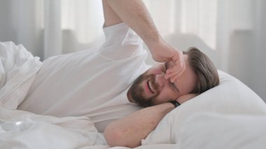 Baş ağrısı olan genç yetişkin bir adam. Yatakta yatıyor.