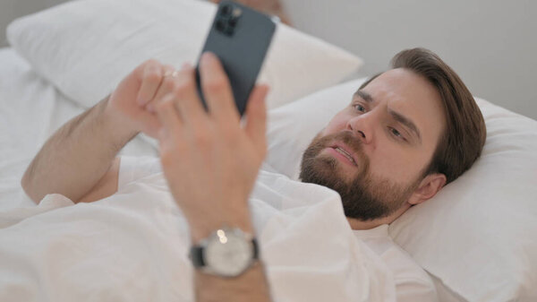 Young Adult Man Shocked by Loss on Phone while Lying in Bed