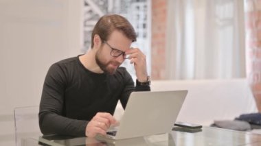 Başı ağrıyan genç yetişkin adam laptopta çalışıyor.