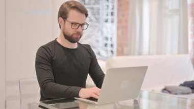 Genç Yetişkin Adam laptopta çalışıyor Kameraya doğru bakıyor