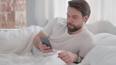 Genç Yetişkin Adam Yatakta Yatıyor ve Telefonu Kullanıyor