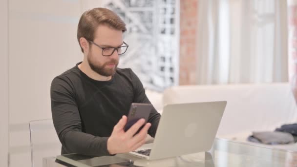 Молодой Взрослый Человек Работает Ноутбуке Помощью Смартфона — стоковое видео
