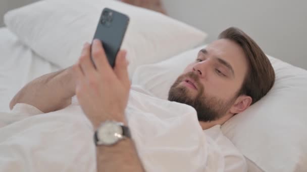 Młody Dorosły Mężczyzna Świętuje Sukces Telefonie Podczas Leżenia Łóżku — Wideo stockowe