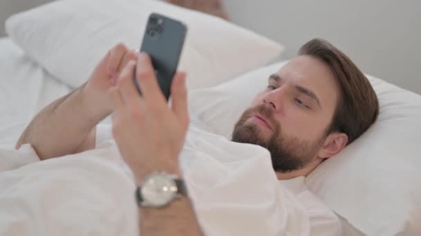 Młody Dorosły Mężczyzna Zszokowany Stratą Telefonu Podczas Leżenia Łóżku — Wideo stockowe