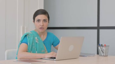 Dizüstü bilgisayarla çalışırken kameraya bakan genç Hintli kadın şok oldu.